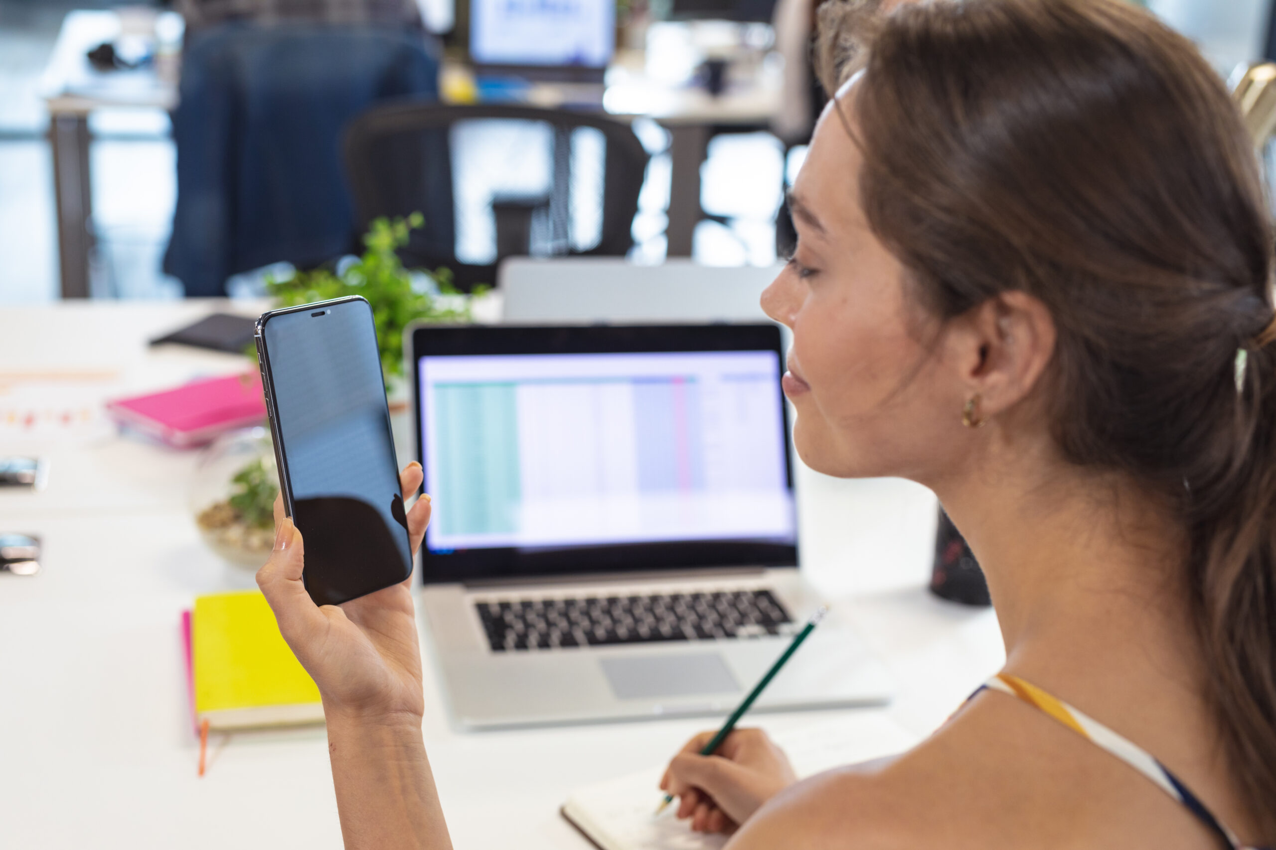 Caucasian female creative worker sitting at desk using smartphone taking notes. modern office of a creative design business.