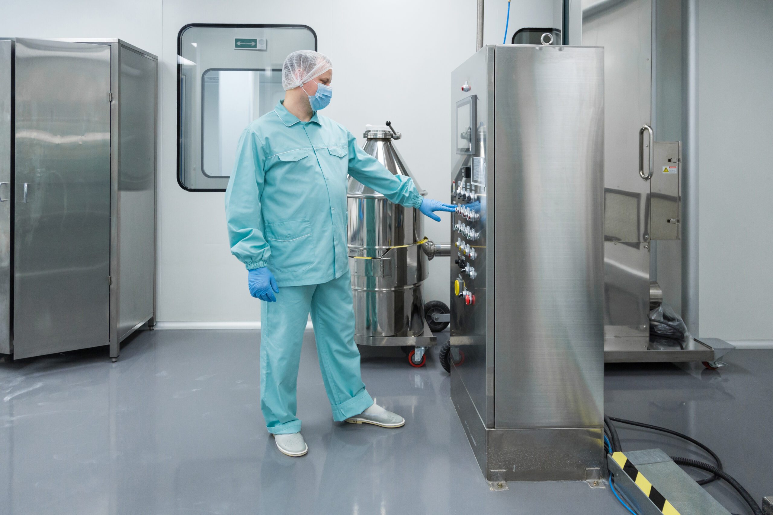 Pharmaceutical factory man worker in protective clothing working with control panel in sterile working conditions