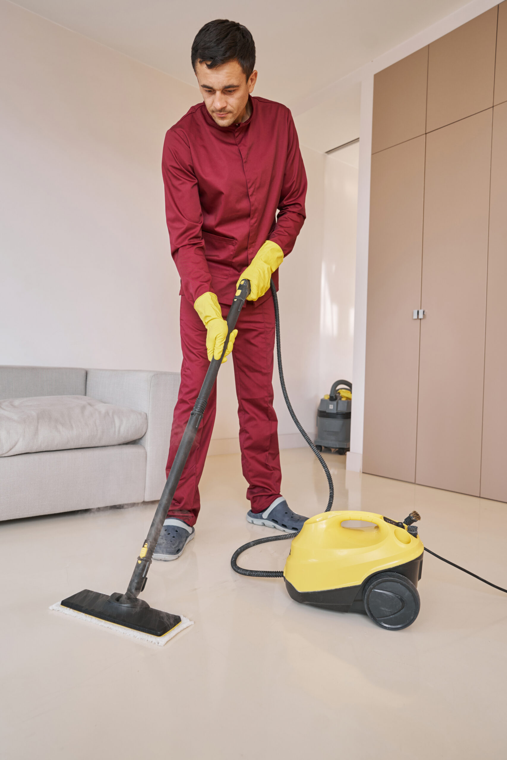 Focused housecleaner in rubber gloves using steam-cleaning appliance